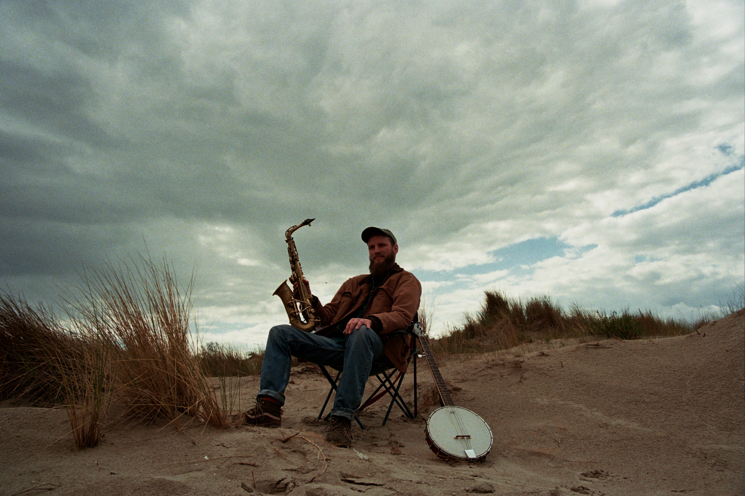 Werend Van Den Bossche seated in the dunes with a saxophone and banjo